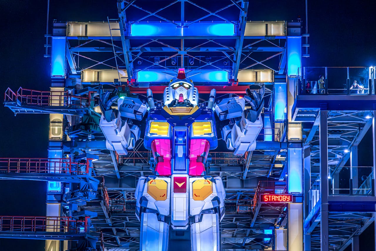 home-img Illuminated Gundam robot at Yokohama's Gundam Factory lit up at night. Vibrant colors and futuristic design.