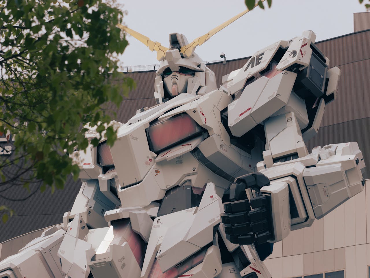 about-img-01 Low-angle shot of the iconic Gundam statue in Tokyo, surrounded by trees, symbolizing modernity.