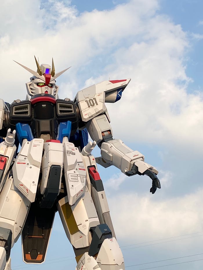 gallery-02 A towering robot statue resembling a Gundam under a bright blue sky, perfect for sci-fi and architecture enthusiasts.